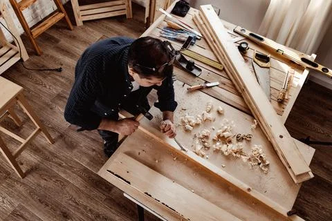 Middle-aged man carpenter working in a workshop with chisel and hammer Stock Photos