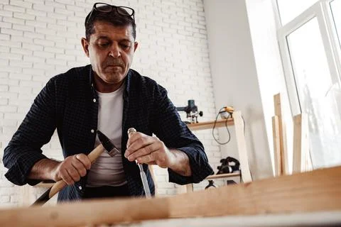 Middle-aged man carpenter working in a workshop with chisel and hammer Stock Photos