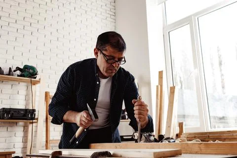 Middle-aged man carpenter working in a workshop with chisel and hammer Stock Photos