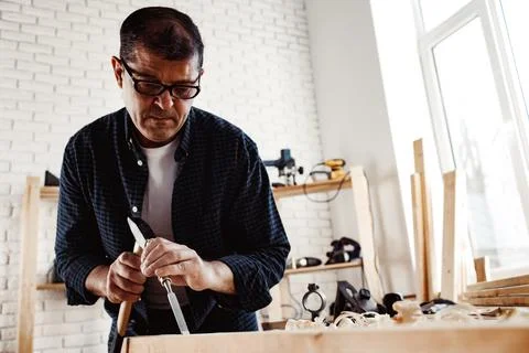 Middle-aged man carpenter working in a workshop with chisel and hammer Stock Photos