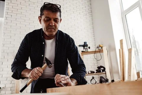 Middle-aged man carpenter working in a workshop with chisel and hammer Stock Photos