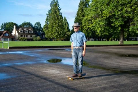 A middle-aged man casually riding on along on a skateboard. Stock Photos