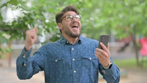 Middle Aged Man Celebrating with Phone Outdoors Видео 311380554