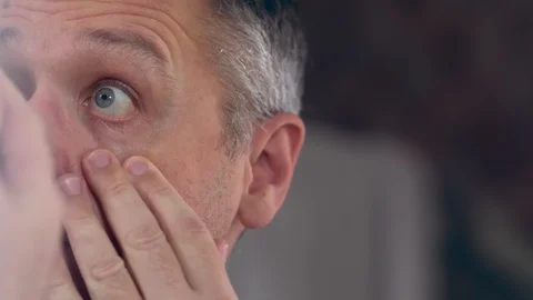 Middle-aged man checking his eyes in a mirror Stock Footage 127932731