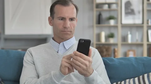 Middle Aged Man Cheering on Smartphone while Sitting on Couch Stock Footage 106958592