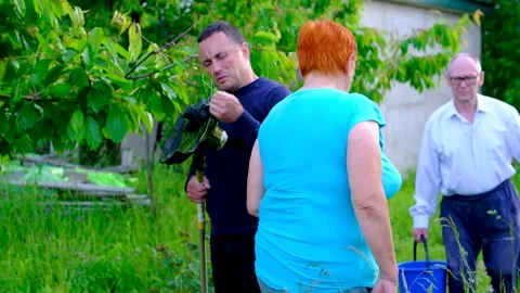 Middle aged man cleaning electric lawn mower after yard work while parents Stock Footage 345327620