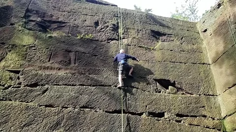 Middle aged man climbing large stone quarry holding cable Stock Footage 254270627
