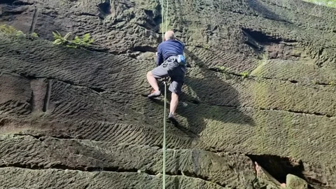 Middle aged man climbing large quarry holding cable Stock Footage 254271421