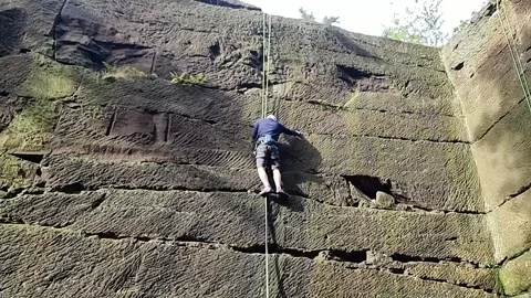 Middle aged man climbing large stone quarry holding cable Stock Footage 254271698