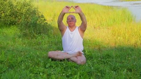 A middle aged man does breathing yoga and meditates on the lake in the morning Stock Footage 118398056