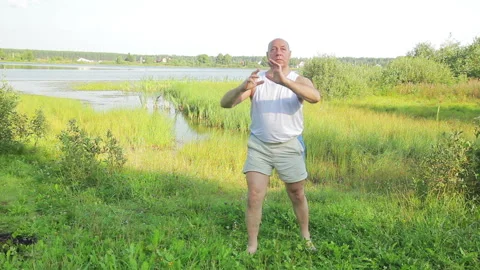 A middle aged man does yoga and breathing exercises on the lake in the morning Vidéo 120869387