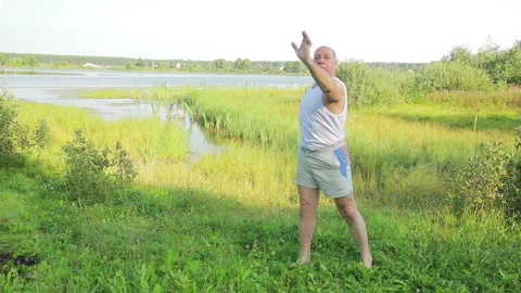 A middle aged man does yoga and breathing exercises on the lake in the morning 库存影片 120869596