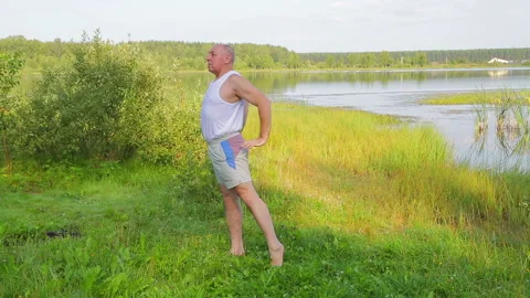 A middle aged man does yoga on breathing exercises on the lake in the morning Vidéo 121018266