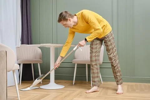 Middle aged man doing housework, mopping floors in living room Foto stock