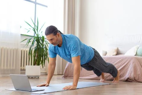 Middle-aged man doing push-ups in front of laptop. He uses an online tutorial Foto stock