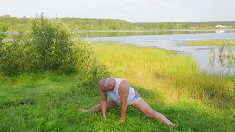 A middle-aged man doing stretching exercises on the lake in the morning Stock Footage 119996144