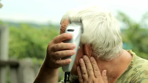 A middle aged man dressed in a khaki t-shirt, shaving his own hair with a Stock Footage 66202932