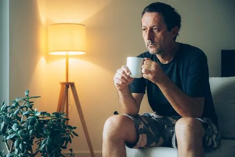 Middle-aged man drinking coffee from a cup in warm living room light, appea.. Stock Photos