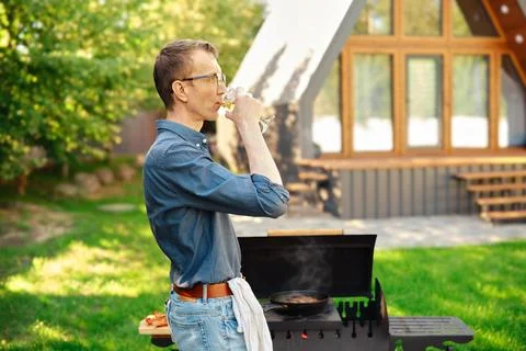 Middle-aged man drinking wine standing near grill in backyard of log cabin Stock Photos