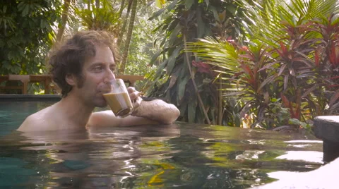 A middle aged man drinks a cup of coffee in an infinity pool at luxury hotel Stock Footage 57816903