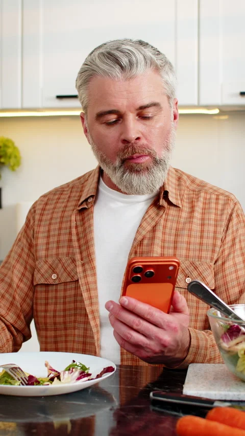 Middle-aged man eating healthy diet salad using smartphone for diet tracking in Stock Footage 347055765