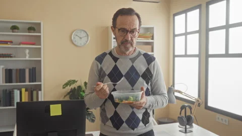 Middle aged man eating salad with fork at computer in office building, hold.. Stock Footage 337442253