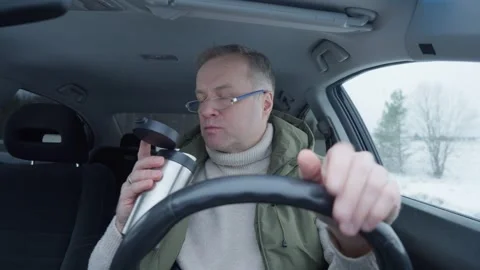 Middle-aged man eats chips and drinks coffee in his car Stock Footage 302889949