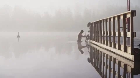 Middle aged man entering cold lake water from wooden dock Stock Footage 346614167