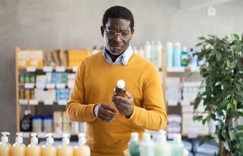 Middle-aged man examining bottle of fever-reducing syrup in pharmacy Stock Photos