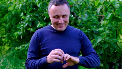 Middle aged man examining rough hands after garden work and smiling at results Stock Footage 345747565