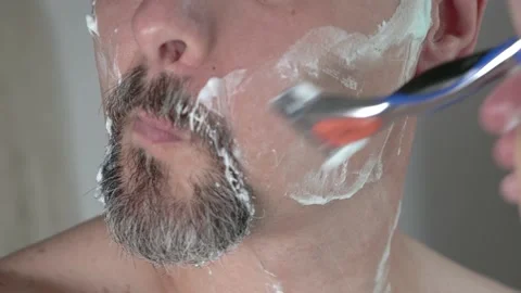 Middle aged man with foam on face shaving beard with a razor, close up 4K Stock Footage 156353154