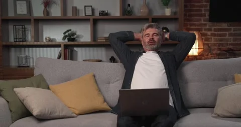 Middle-aged man freelancer relaxing on the couch from working on a laptop Video stock 210188216