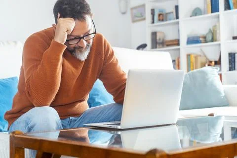 Middle-aged man frustrated while working on laptop at home living room with.. 스톡 사진