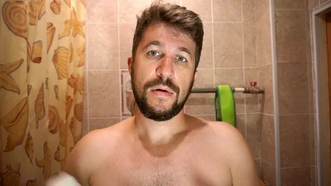 Middle aged man with a full beard applies shaving cream to his face Vídeos de archivo 93819060