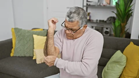 Middle-aged man with glasses and grey hair feels elbow pain while sitting o.. Stock Footage 263889194