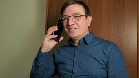 A middle-aged man with glasses puts his smartphone to his ear Stock Footage 150695099
