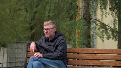 Middle aged man with glasses is sitting on bench in city park. urban lifestyle. Stock Footage 250949190