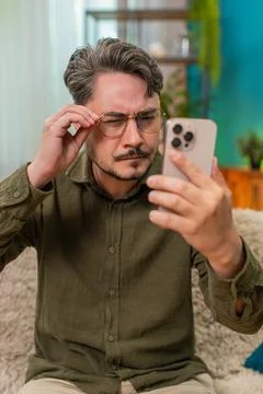 Middle-aged man in glasses squints reading tiny smartphone text checking Stock Photos