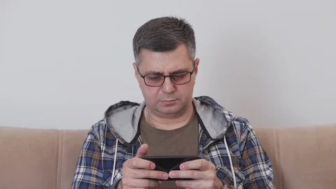 A middle aged man in glasses is using mobile internet in a smartphone while Stock Footage 104588213