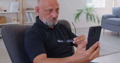 Middle aged man grabs reading glasses while squinting at smartphone screen Stock Footage 318368578
