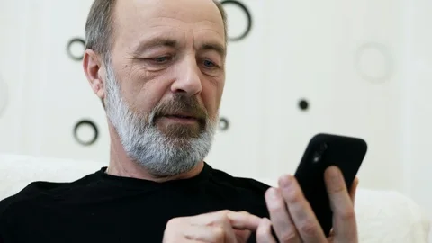 Middle-aged man with a gray beard uses the phone at home, close-up Stock Footage 124618390