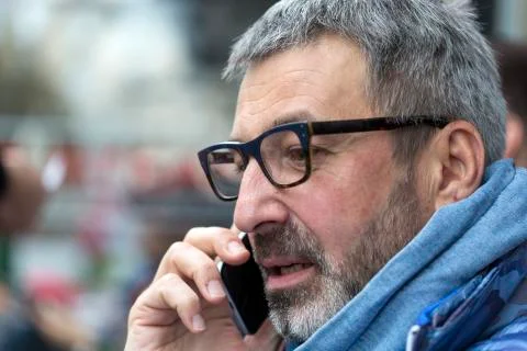 Middle-aged man with a gray beard and urban glasses, talking on a mobile phon Stock-Fotos