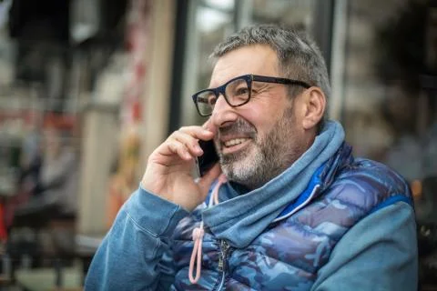 Middle-aged man with a gray beard and glasses talking on a mobile and smile Stock-Fotos