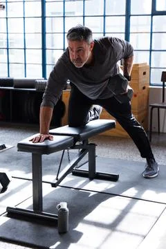Middle-aged man in gray top performing bent-over row pulling hex dumbbell Stock Photos