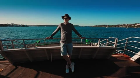 A middle-aged man in a hat and sunglasses stands on the deck of a Sydney city Stock Footage 308319206