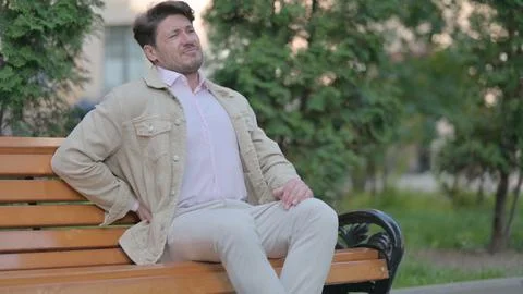 Middle Aged Man Having Back Pain while Sitting Outdoor on a Bench Stock Photos
