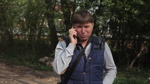 A middle-aged man in his 50s is talking on the phone outside in a park Stock Footage 109160113