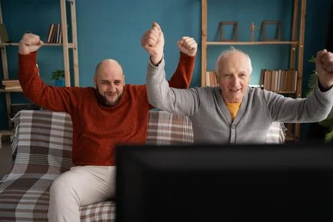 Middle-aged man with his elderly father watching sports at home Stock Photos