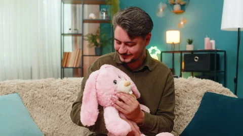 Middle-aged man holding pink bunny toy smiling sadly missing child remembering Stock Footage 316958742