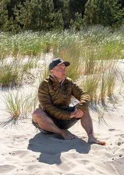 Middle-aged man in jacket and shorts sits on sand Baltic Sea. Soft sand dun.. Stock Photos